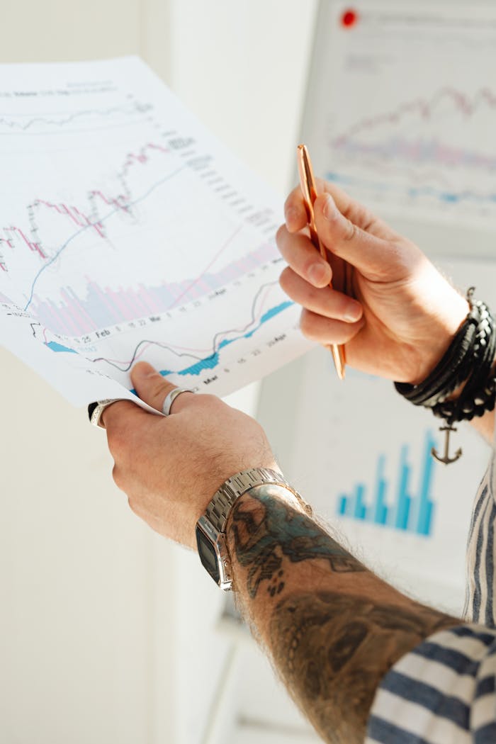 Close-up of a persons hands holding financial charts and graphs with a pen.